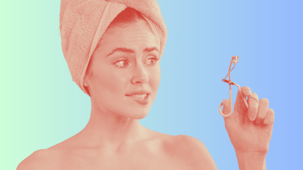 woman on bright background with eyelash curler and her hair in a towel