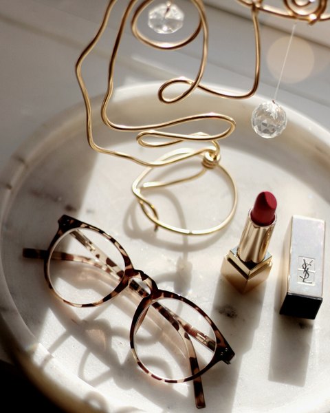 Lipstick, tortoiseshell glasses, and gold decor on a marble tray