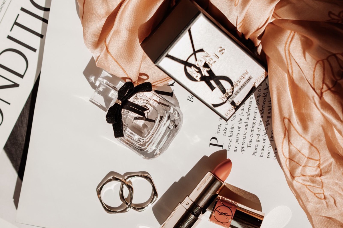 Perfume, lipstick, and gold rings styled on an open magazine in warm light