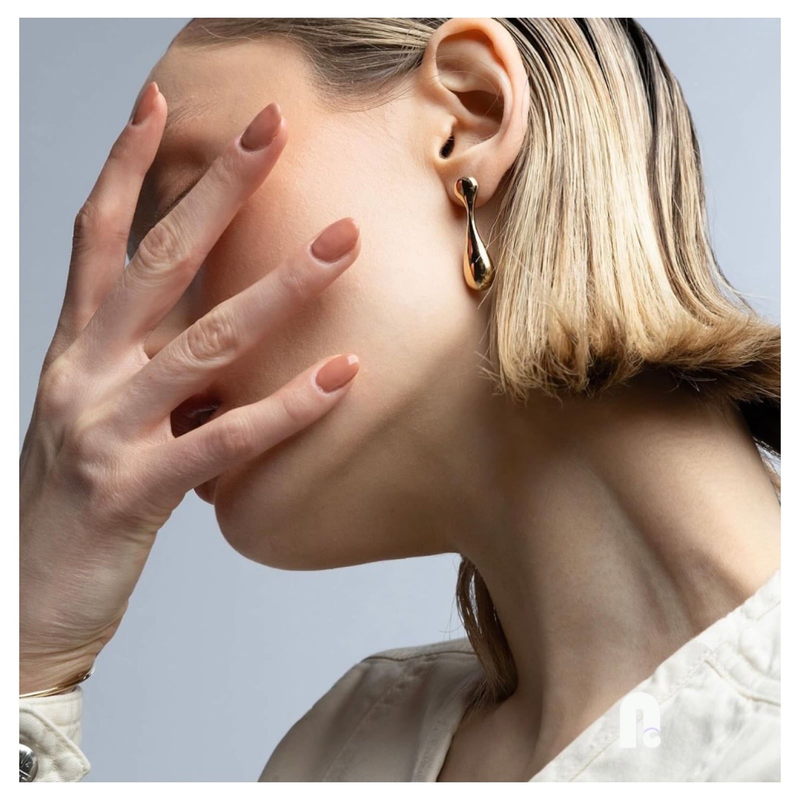 Peachy nude almond nails on a light-skinned hand held against a model's face