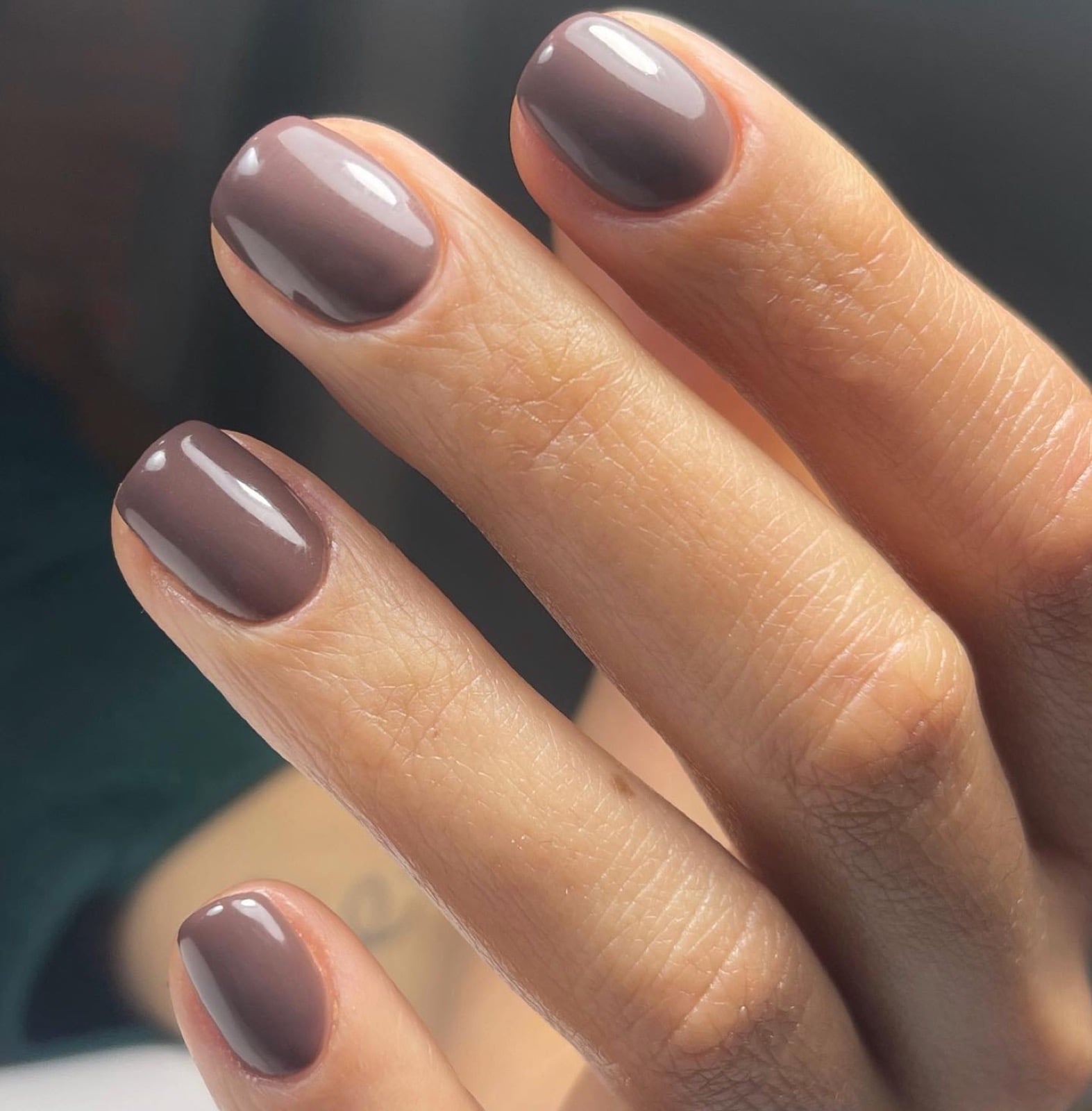 Short taupe manicure on a medium olive-toned hand